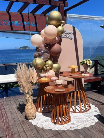 Decoração de aniversário com balões dourados e mesas de madeira com vista para o mar